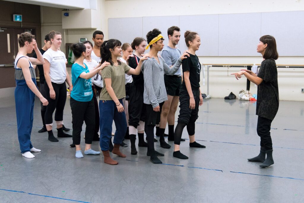 Students with hands on the shoulders of the person infront of them, standing before Hanna Kiel, mentor.